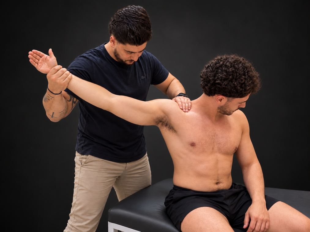 Fisioterapeuta realizando mobilização de ombro em atleta sentado na maca